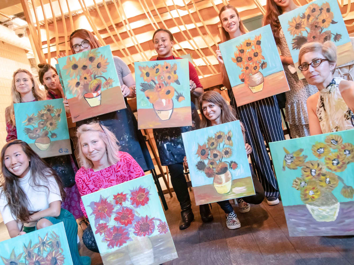Mother's Day Ideas - sip and paint themed around Van Gogh's Sunflowers. Photo shows a group of people holding up their finished paintings