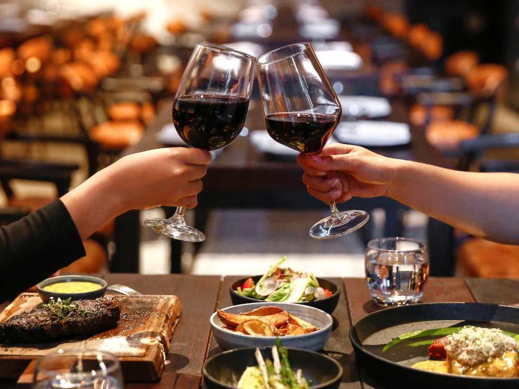 Valentine's Day Date Ideas - dinner: two people clinking glasses of red wine at the dinner table in a restaurant